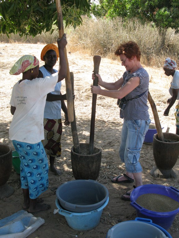 Women pounding grain with a wooden mortar and pestle in a Gambian village